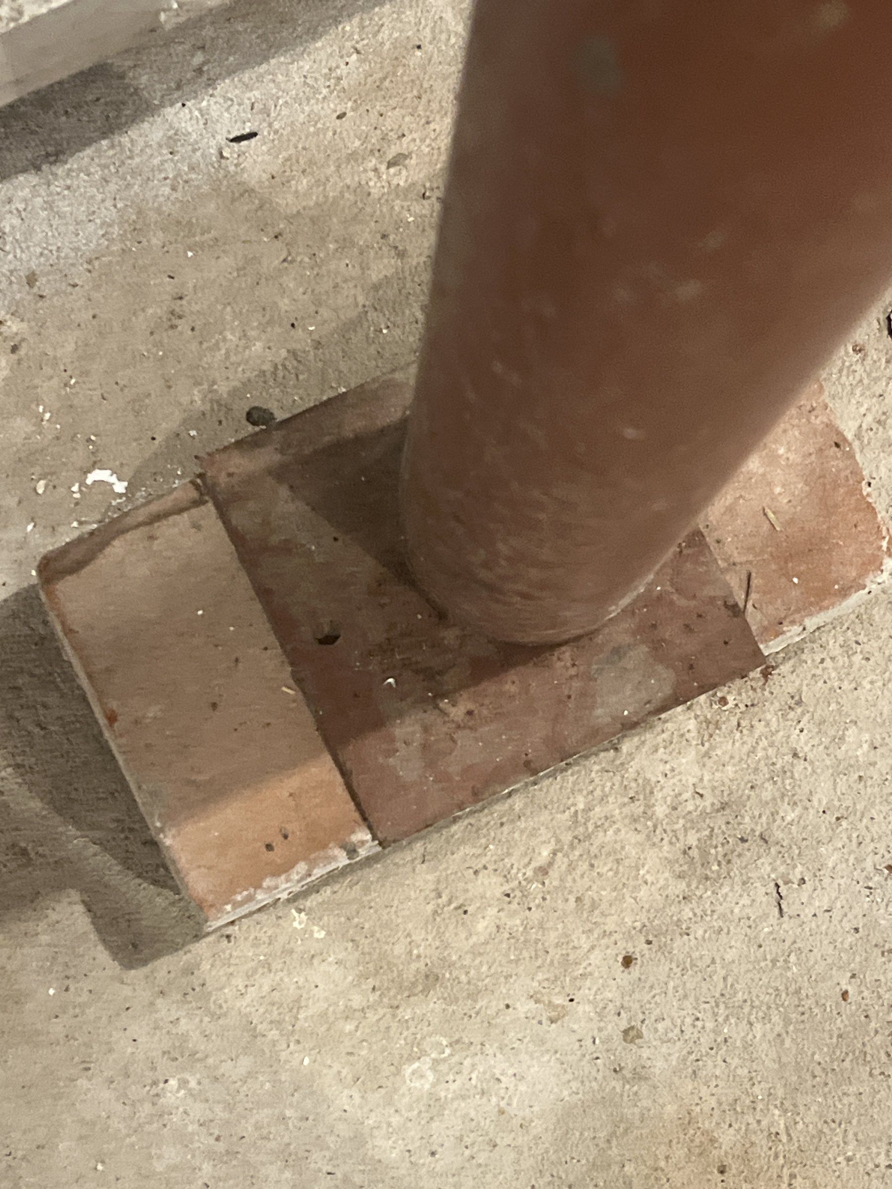 Base of a two-piece adjustable steel post standing on a loose brick laid on a basement slab