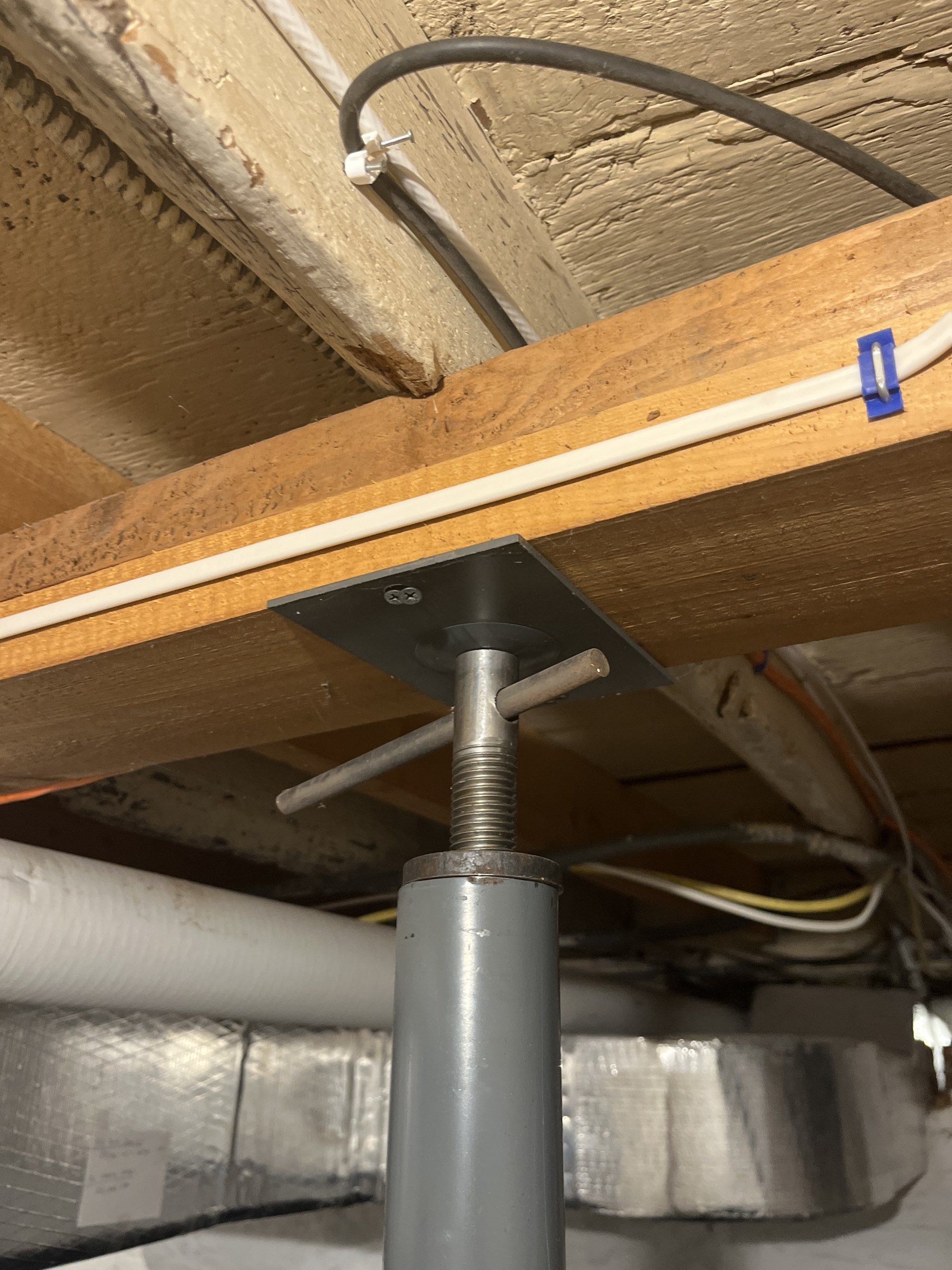 Top of a two-piece adjustable steel post with the adjusting screw exposed and the small plate held to the beam with two screws