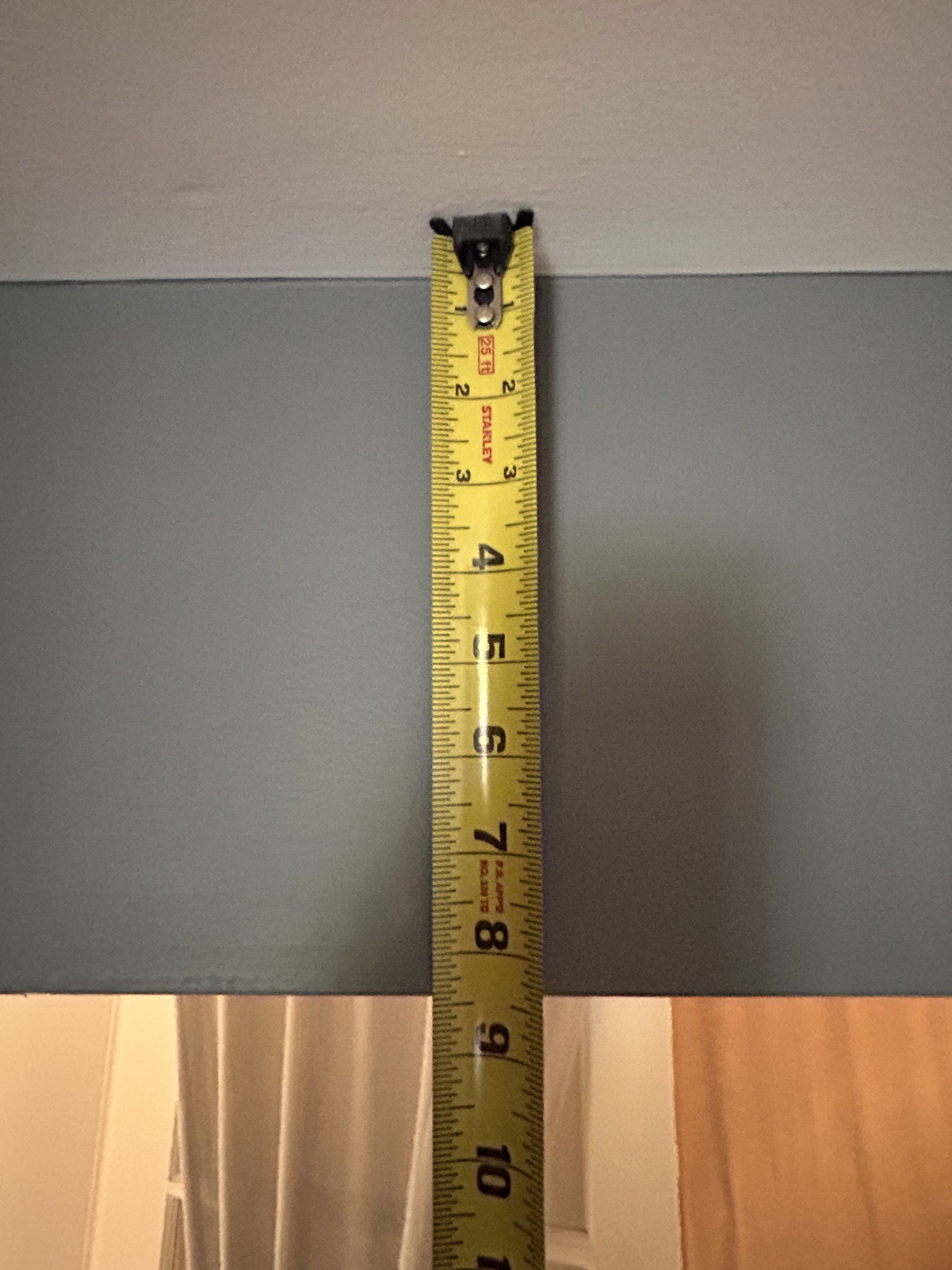 Tape measure hanging down the face of a boxed carrying beam in a finished basement ceiling
