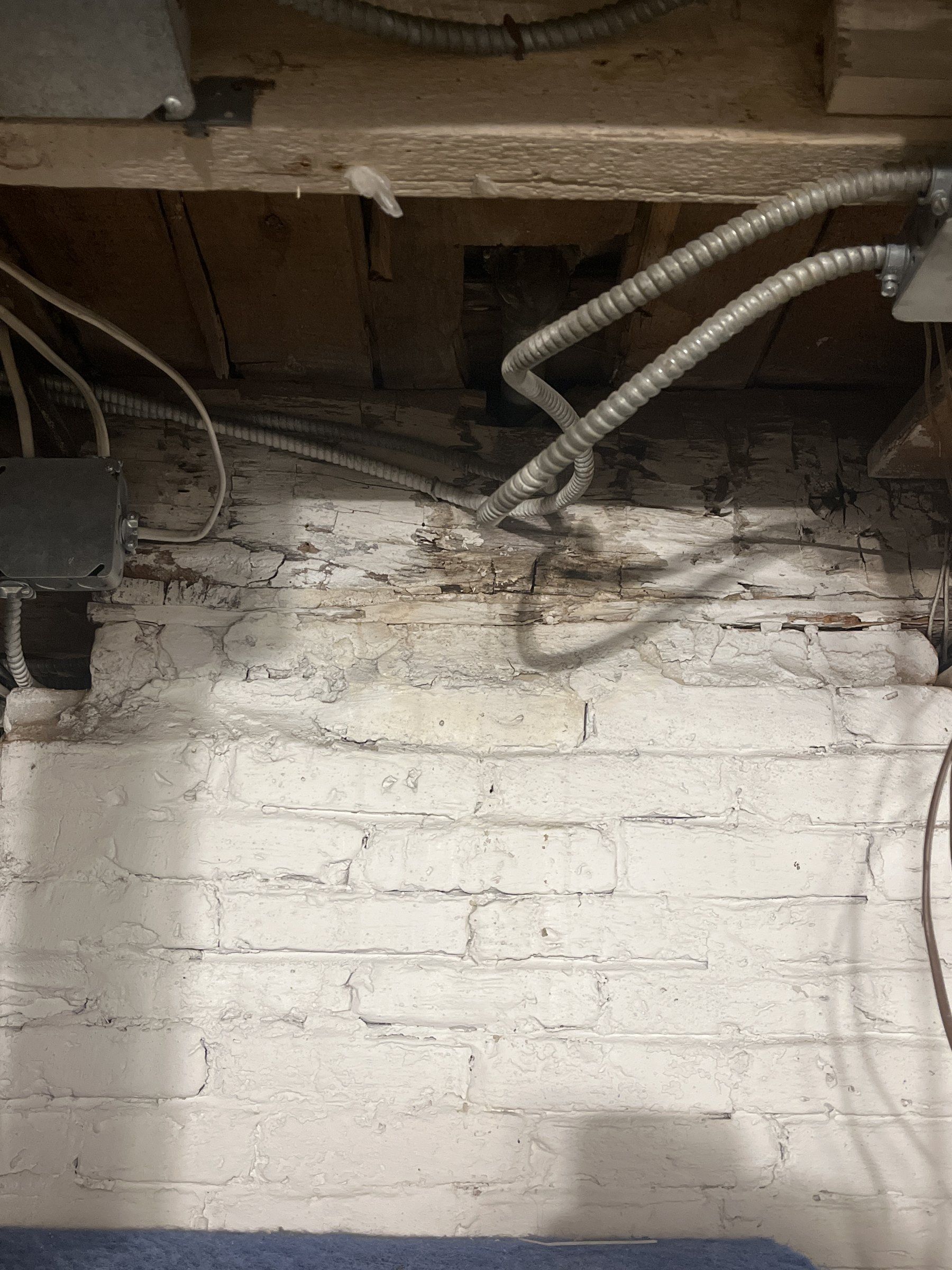 Weathered hewn girt resting on top of an interior brick wall in the basement of a 1790s house, with joists hung from its face