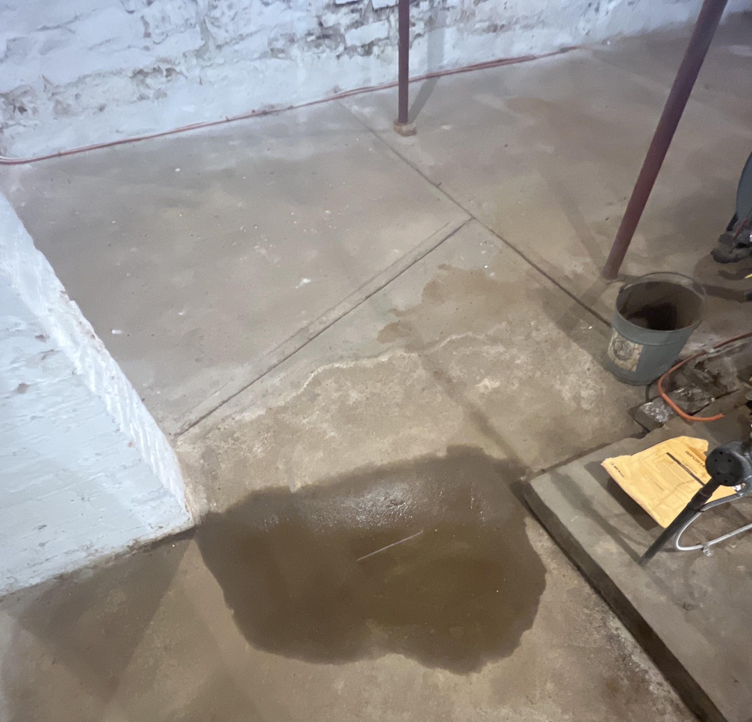 Shallow standing water on a concrete basement slab beside a brick pier in an old house